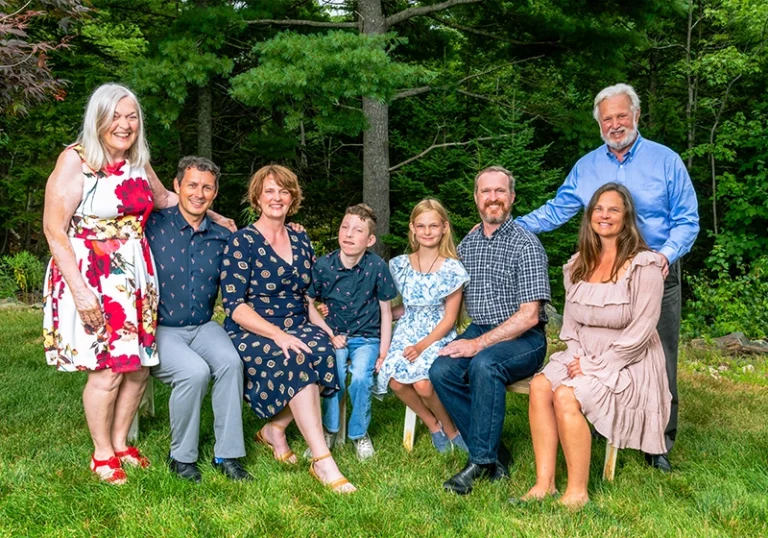 Grandparents posing with their children and grandchildren in a natural outdoor setting, captured by a Family Portrait Studio. The family is gathered closely together, smiling and enjoying a multi-generational moment.