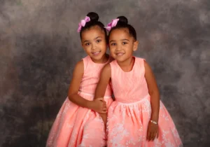 Twin girls wearing matching dresses, posing sweetly together in a professional Family Portrait Studio, capturing their bond and playful energy