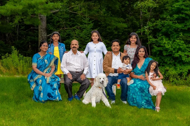 Mother and father sitting on a bench with their children, captured together in a joyful family portrait in an outdoor setting at a Family Portrait Studio.