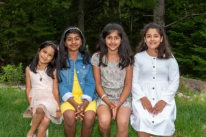 Four sisters sitting together on a bench in the outdoor settings of a Family Portrait Studio, enjoying a playful and bonding moment surrounded by nature.