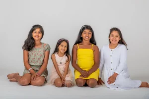 Four sisters sitting on their knees in a Family Portrait Studio, posing together with smiles, capturing a fun and close-knit sibling moment.