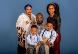 Father sitting on a stool with his wife and mother standing behind him, and two kids sitting on his lap, captured together in a warm family moment at a Family Portrait Studio.